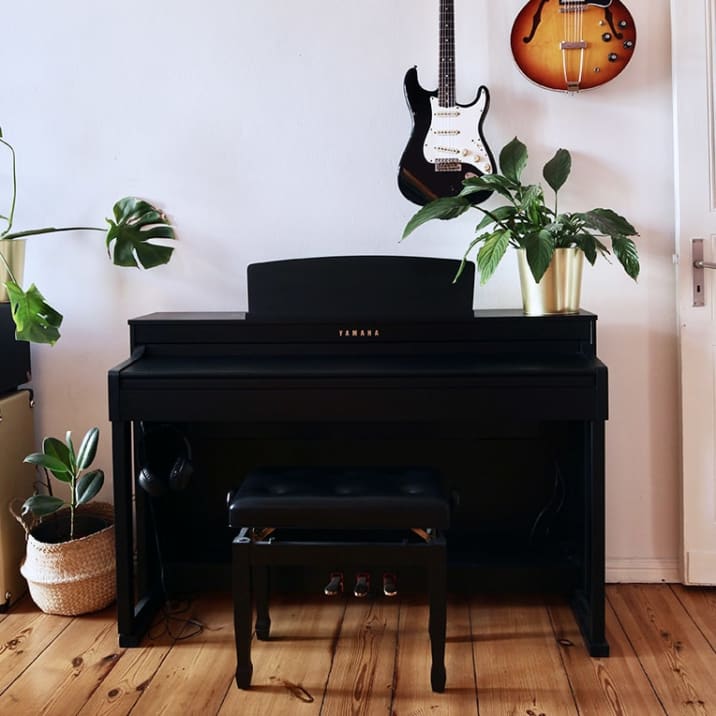 A monstera, peace lily and rubber plant placed on and around a black piano in a living room