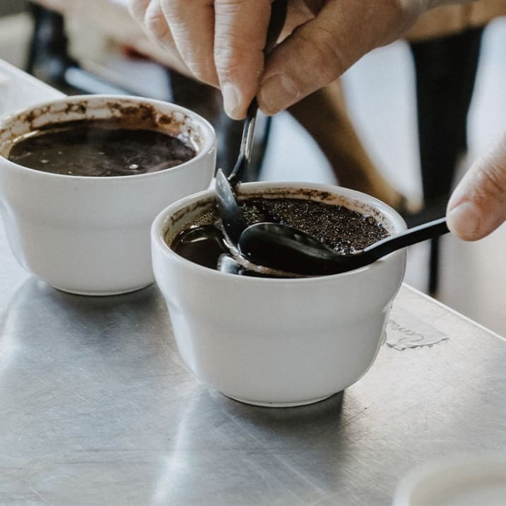 Coffee grounds being scooped out of a bowl with two spoons