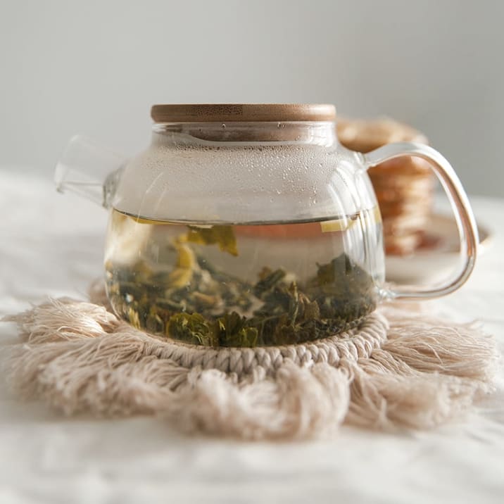 Green tea leaves brewing in water inside of a glass kettle