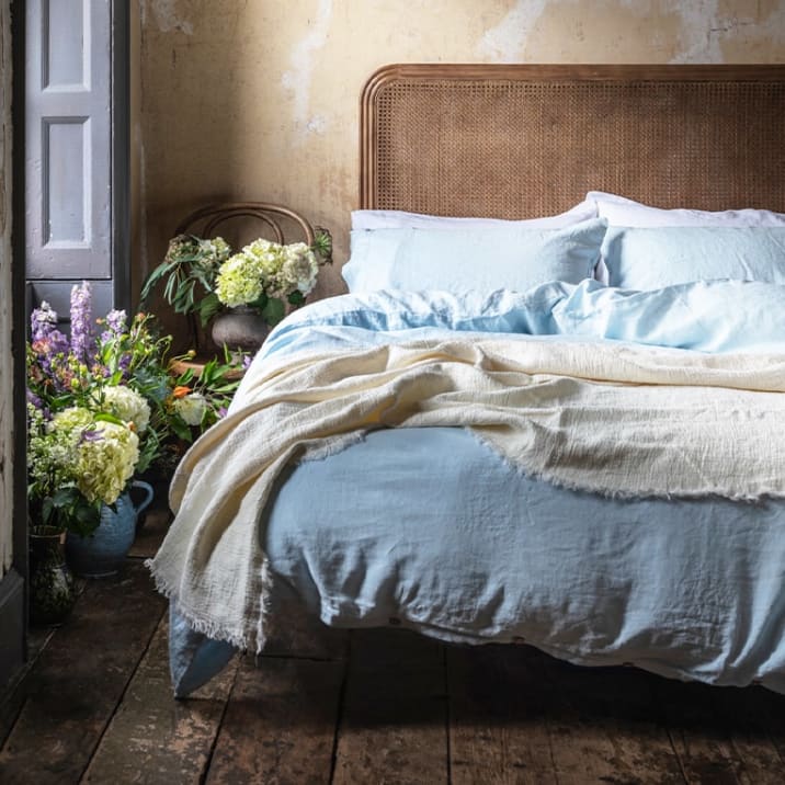 A bed dressed in light blue bedlinen in a bedroom