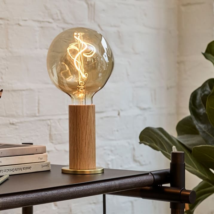 Lamp on a side table with a swirled filament next to a fiddle-leaf fig