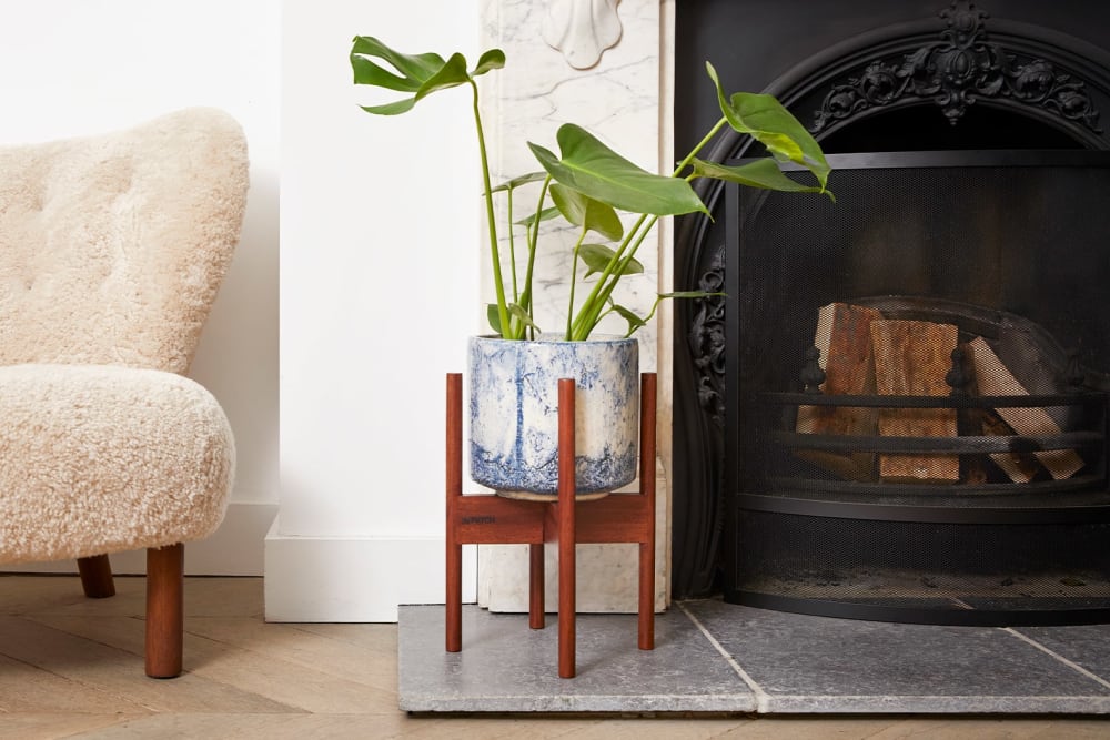 A monstera in a blue fractured ceramic pot in a plant stand in a living room