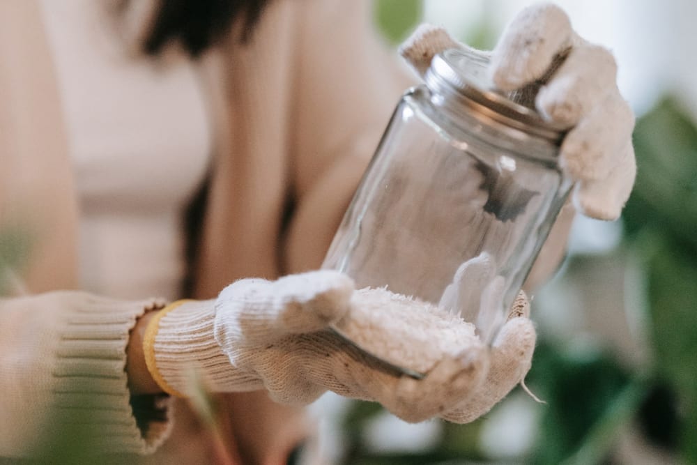A woman wearing gloves holding a glass jar containing a white rocky substance